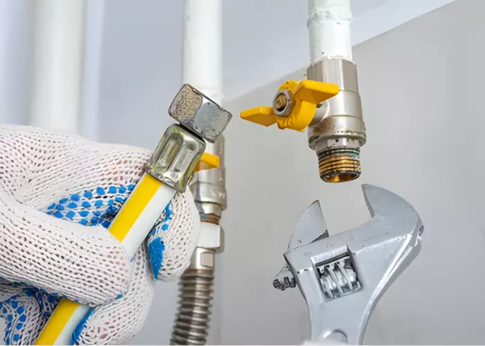 A technician wearing gloves uses a wrench to tighten a gas valve.