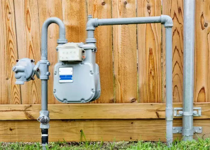 A natural gas meter is attached to a wooden fence.