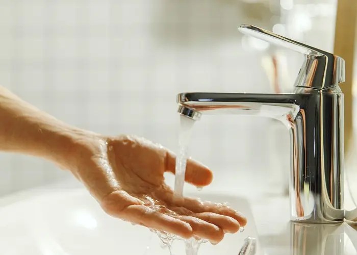 A person washes their hands under a faucet with running hot water.