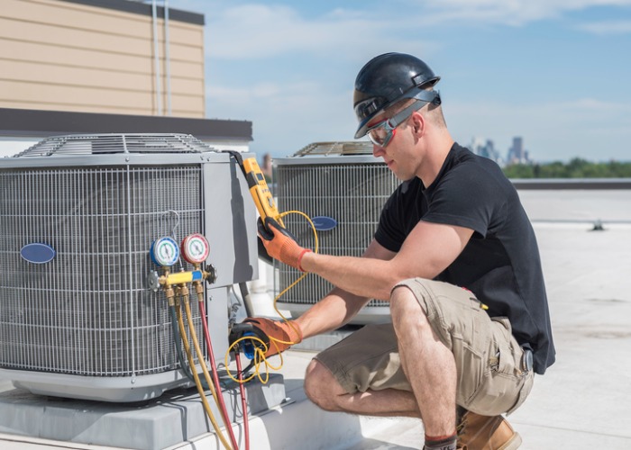 An HVAC technician repairs an air heater unit on a building rooftop.
