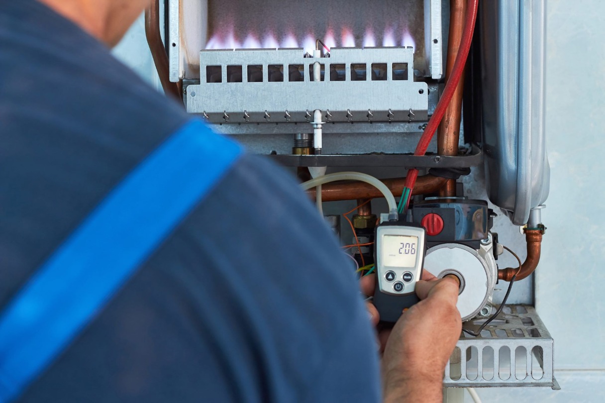 A man checks a digital thermometer next to a furnace.