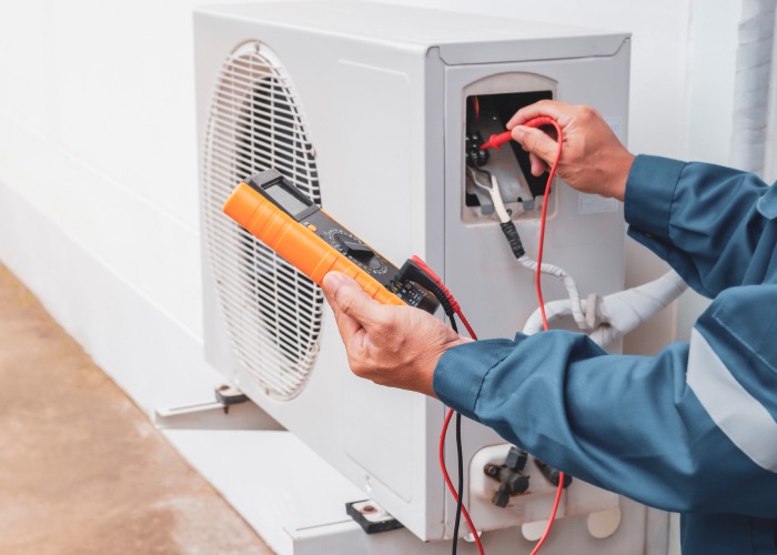 An HVAC technician is using a multimeter to check the electrical voltage of an air conditioner.